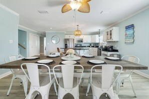 Une cuisine moderne avec des meubles blancs, un îlot central et un coin repas comprenant des chaises blanches et une table en bois.