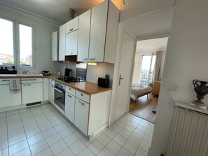 A compact kitchen with white cabinets, a stove, and a coffee maker. - Nid d Aigle, 2 Stations from Paris, Charming Top Floor Apartment Bright, Fully Equipped, Washing Machine High Speed Fibre WiFi (Bois-Colombes)