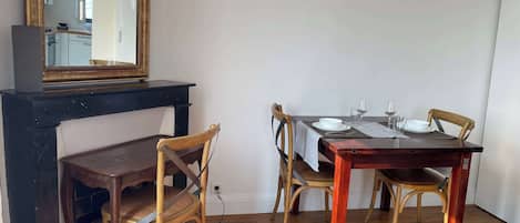 A dining area with a wooden table, four chairs, a mirror above the table, and a fireplace below.