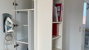 Ein weißer Kleiderschrank mit Einlegeböden, einem gebügelten Bügeleisen und einer Steckleiste.