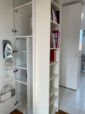Ein weißer Kleiderschrank mit Einlegeböden, einem gebügelten Bügeleisen und einer Steckleiste.