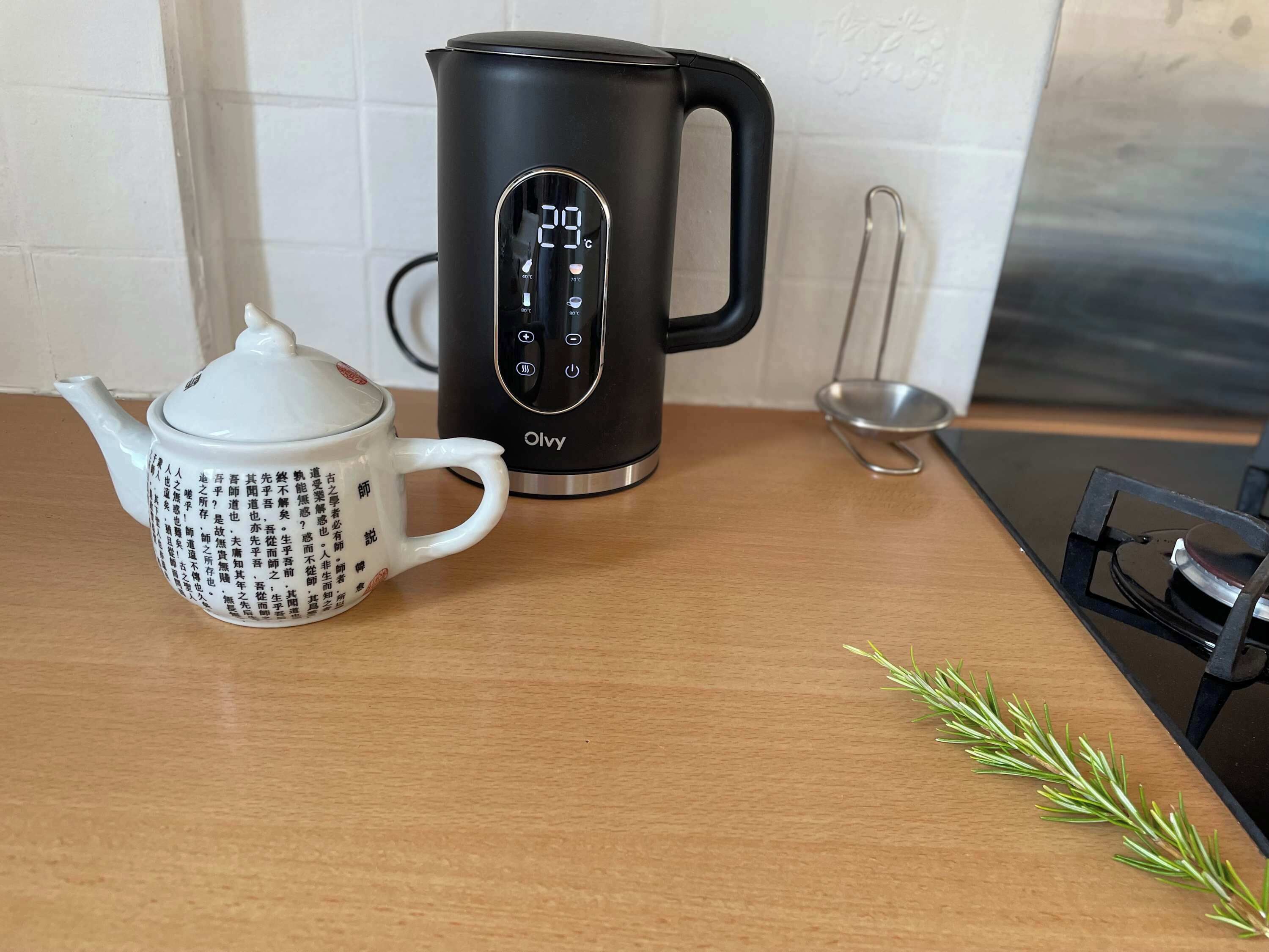 Ein schwarzer elektrischer Wasserkocher mit digitaler Anzeige und eine weiße Teekanne mit chinesischen Schriftzeichen auf einem Holztisch.