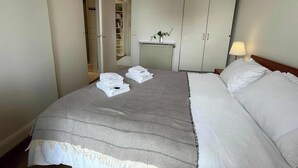 Ein Hotelzimmer mit Bett, Nachttisch mit Lampe, Kleiderschrank und einem durchgegangenen Tür angedeuteten Badezimmer.