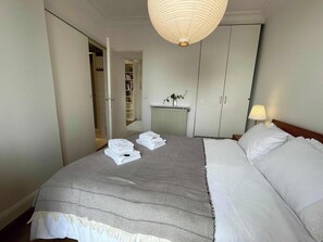 Ein Hotelzimmer mit Bett, Nachttisch mit Lampe, Kleiderschrank und einem durchgegangenen Tür angedeuteten Badezimmer.