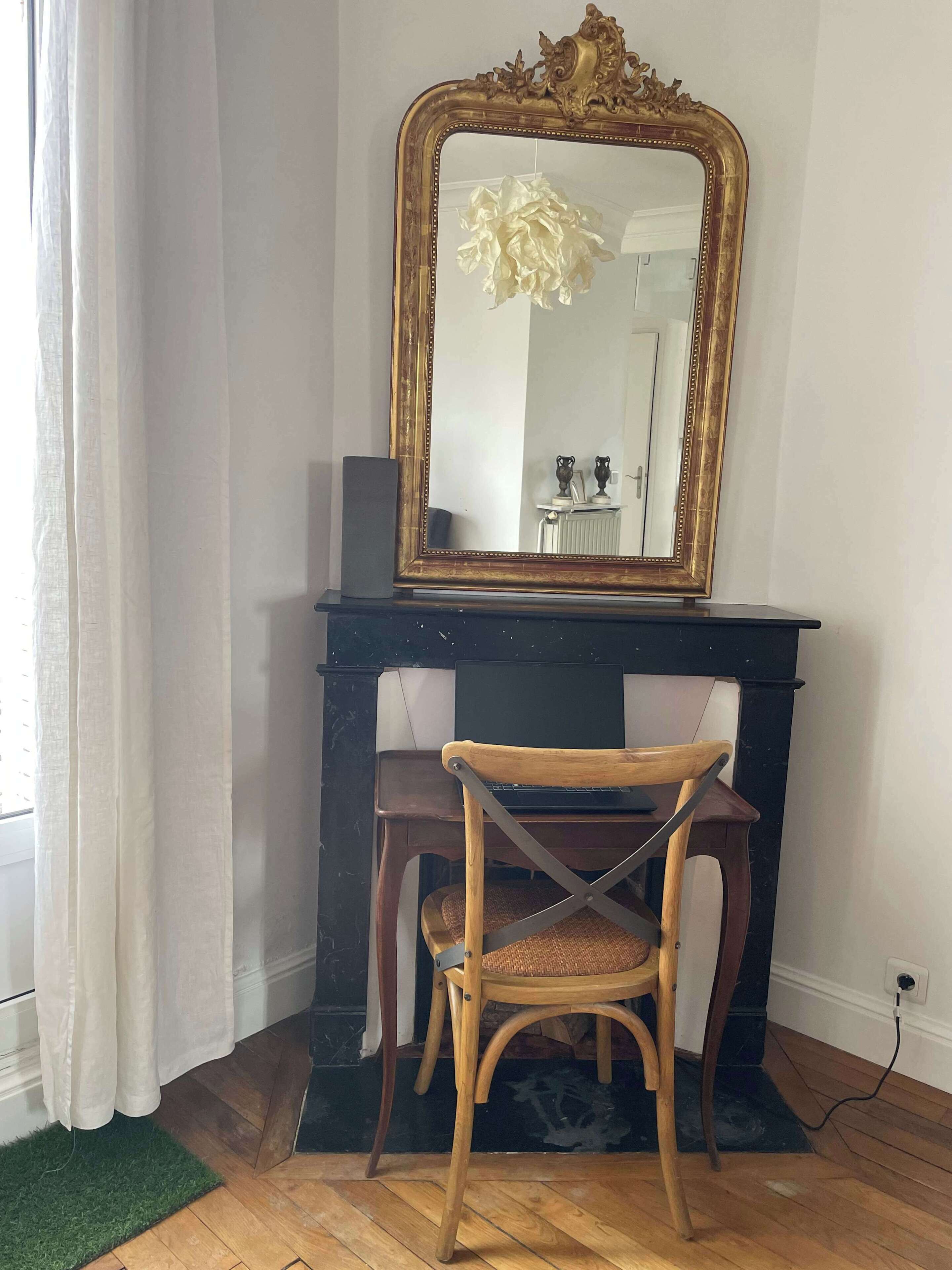 A room with a wooden desk, a chair, a large mirror with an ornate frame, and a radiator.