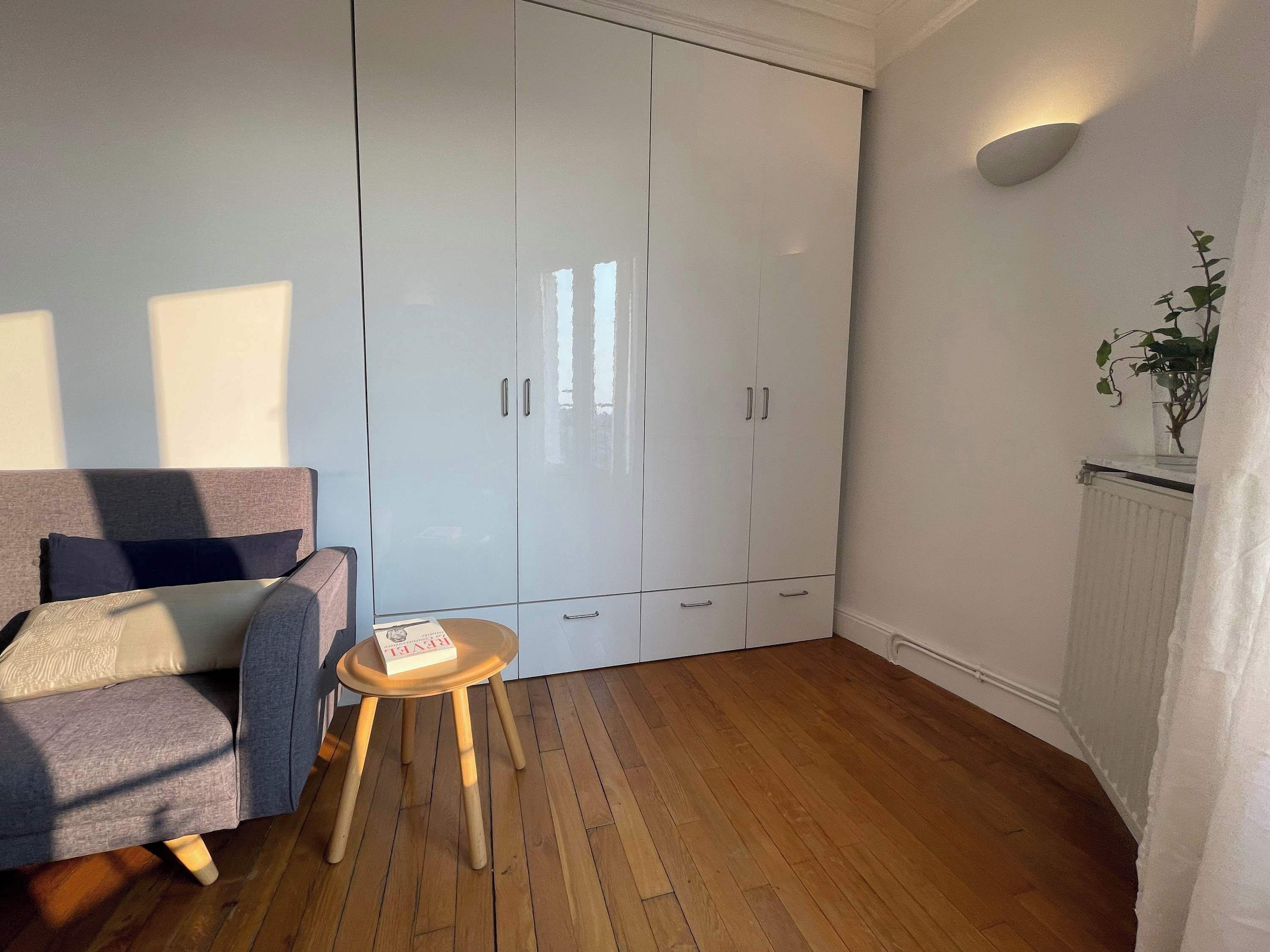 Une pièce avec un canapé gris, une petite table en bois, une armoire blanche et une plante en pot.