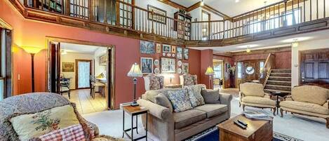 A spacious living room with a high ceiling, a staircase, and a balcony.