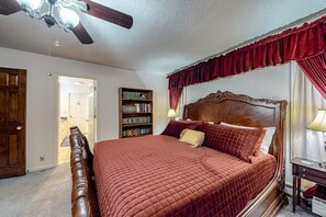 A bedroom with a large bed, a wooden headboard, a ceiling fan, a bookshelf, and a door leading to another room. - Dragonfly Estate - the Main House & Studio (South Fork)