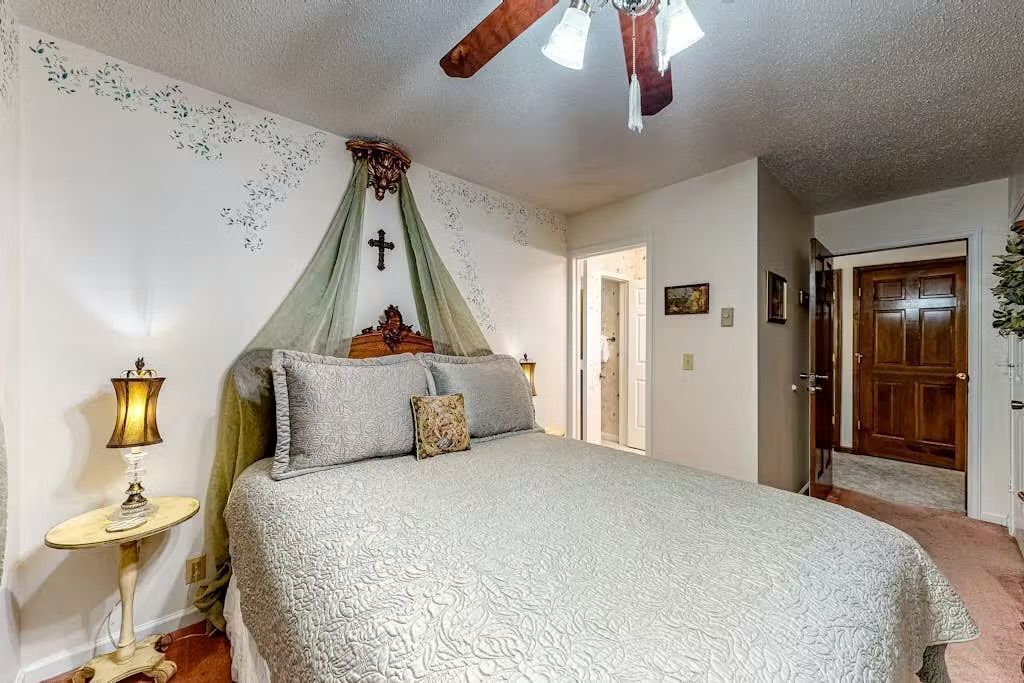 A bedroom with a bed, a nightstand, a cross on the wall, and a door.
