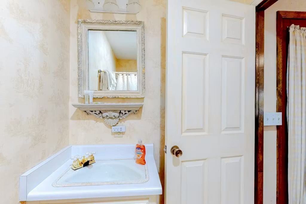 A bathroom with a white sink, a mirror with a decorative frame, and a door with a wooden panel.