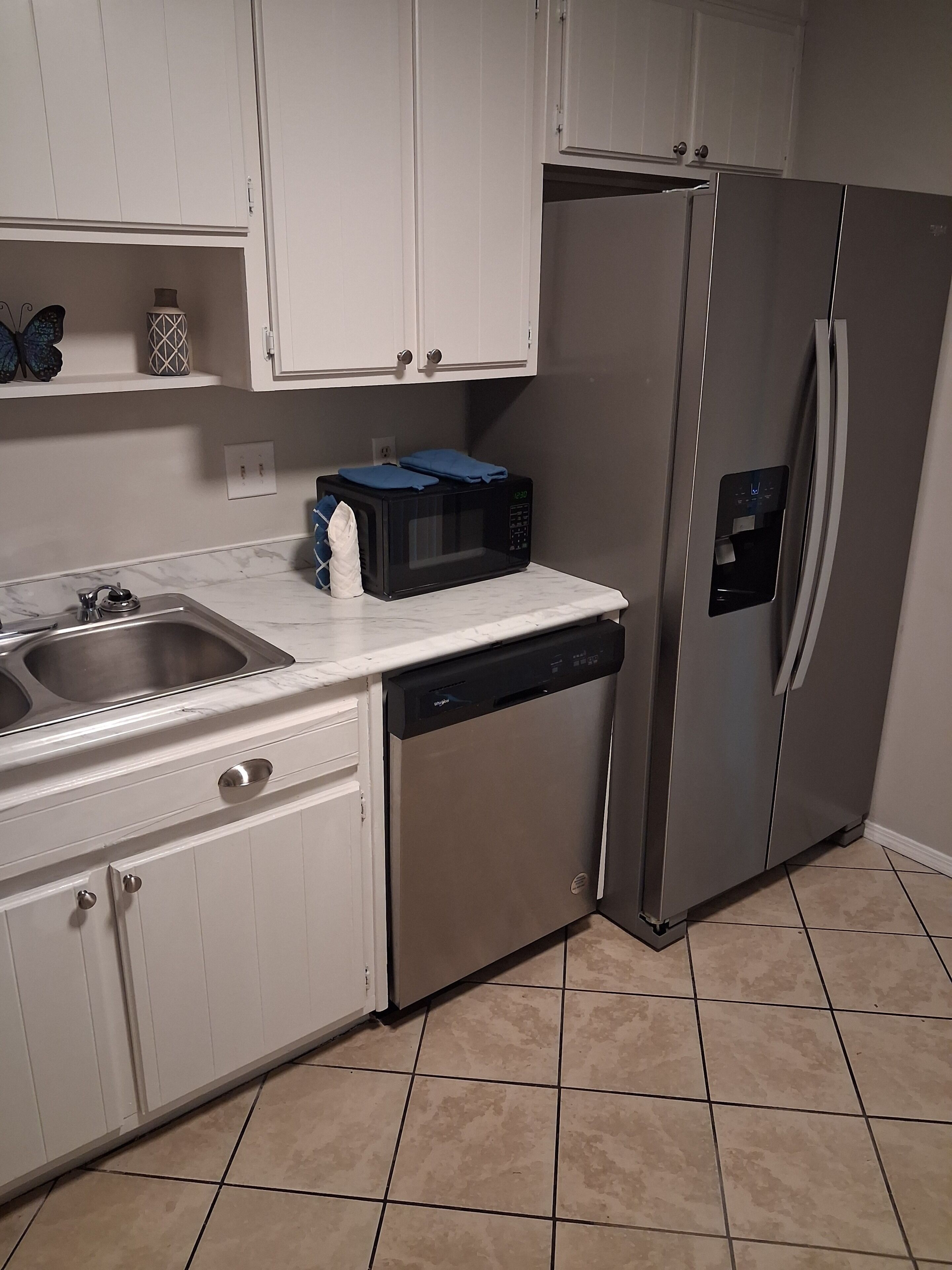 A kitchen with white cabinets, a stainless steel refrigerator, a microwave, and a dishwasher.