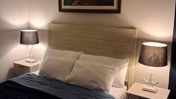 Un dormitorio con cama, dos lámparas de noche, un cuadro enmarcado en la pared y una alfombra estampada.