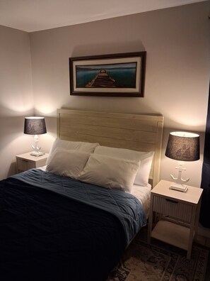 A bedroom with a bed, two bedside lamps, a framed picture on the wall, and a patterned rug.