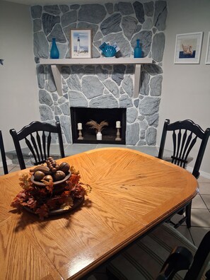 A dining area with a stone fireplace, a wooden table, and two chairs.