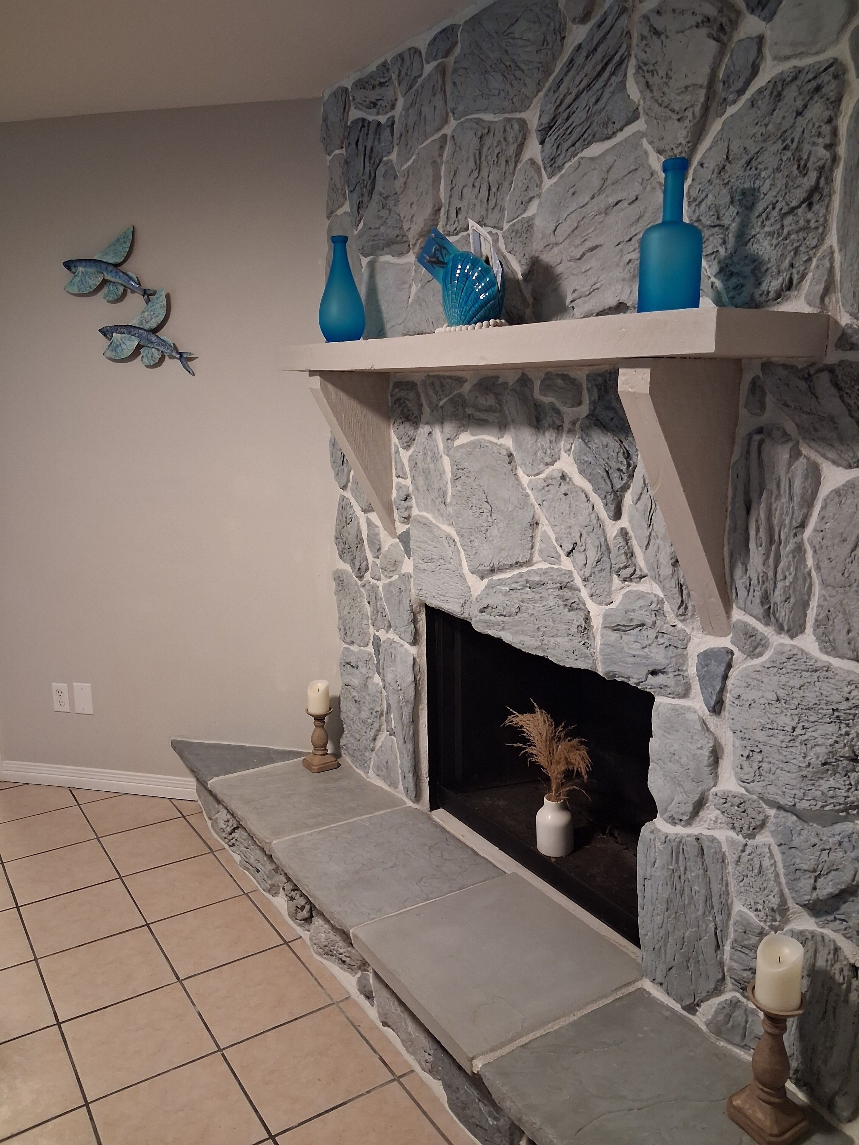 Une cheminée en pierre avec une étagère décorative, un sol carrelé et un élément décoratif fixé au mur.