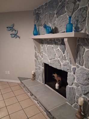 A stone fireplace with a mantel shelf, a tiled floor, and a wall-mounted decorative piece.