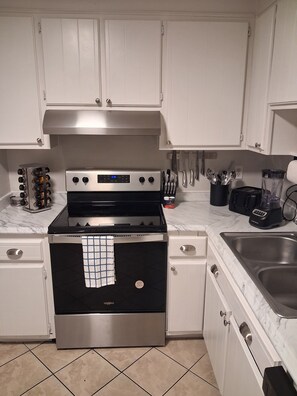 A kitchen with white cabinets, a stainless steel stove, a sink, and a marble countertop.