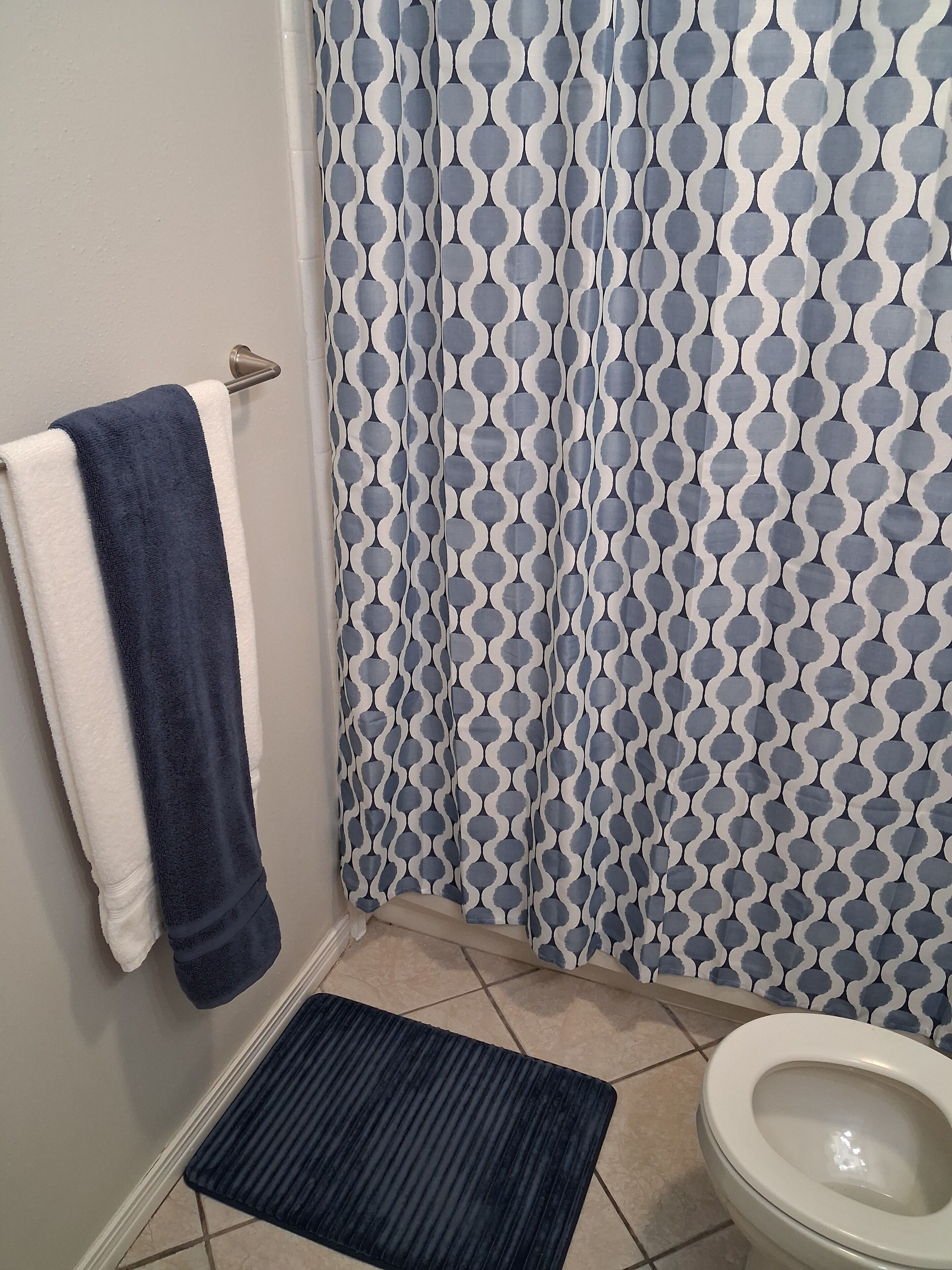 A bathroom with a patterned shower curtain, a white toilet, and a dark blue towel on a rack.