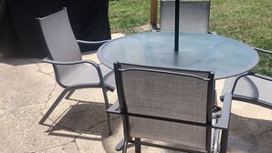 An outdoor patio with a round table and two chairs, a covered grill, and a wooden fence in the background.