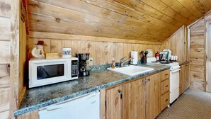 A compact kitchen with wooden walls, a granite countertop, a microwave, a coffee maker, a sink, and a dishwasher. - The Dragonfly  Studio (South Fork)