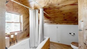 A wooden cabin bathroom with a bathtub, toilet, and a window. - The Dragonfly  Studio (South Fork)
