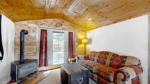 A wooden interior with a sofa, a table, a lamp, and a wood-burning stove. - The Dragonfly  Studio (South Fork)