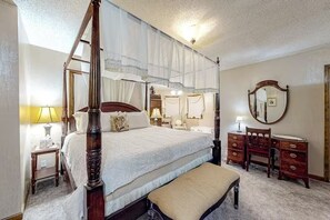 Un lit à baldaquin à quatre poteaux, avec un banc, une commode, un miroir et une table de chevet avec une lampe.