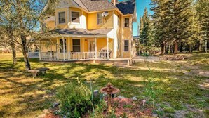 A two-story house with a porch, surrounded by a grassy yard and trees. - The Dragonfly Main House (South Fork)