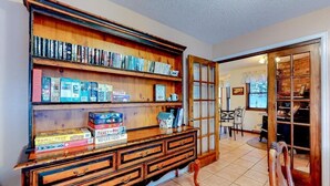 A room with a wooden bookcase filled with books, a wooden chest of drawers, and a dining area visible through an open door. - The Dragonfly Main House (South Fork)