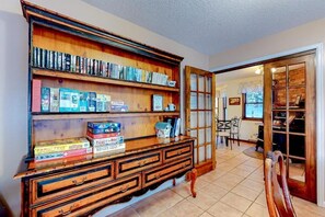 A room with a wooden bookcase filled with books, a wooden chest of drawers, and a dining area visible through an open door. - The Dragonfly Main House (South Fork)