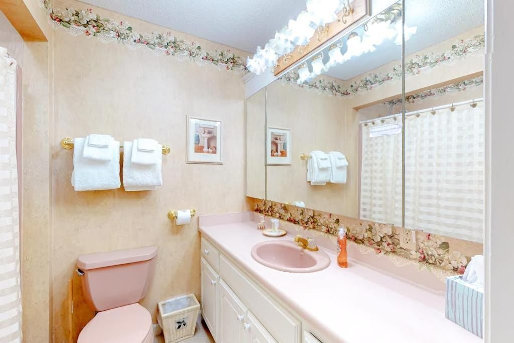 Et badeværelse med toilet i pink, en vaskepult med pink vask og et spejl med lys.