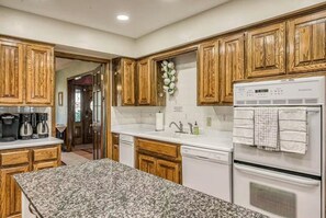A kitchen with wooden cabinets, granite countertops, a refrigerator, and a dishwasher. - The Dragonfly Main House (South Fork)