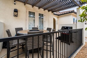 Un patio exterior con una mesa redonda, sillas de mimbre, una parrilla y una pérgola.