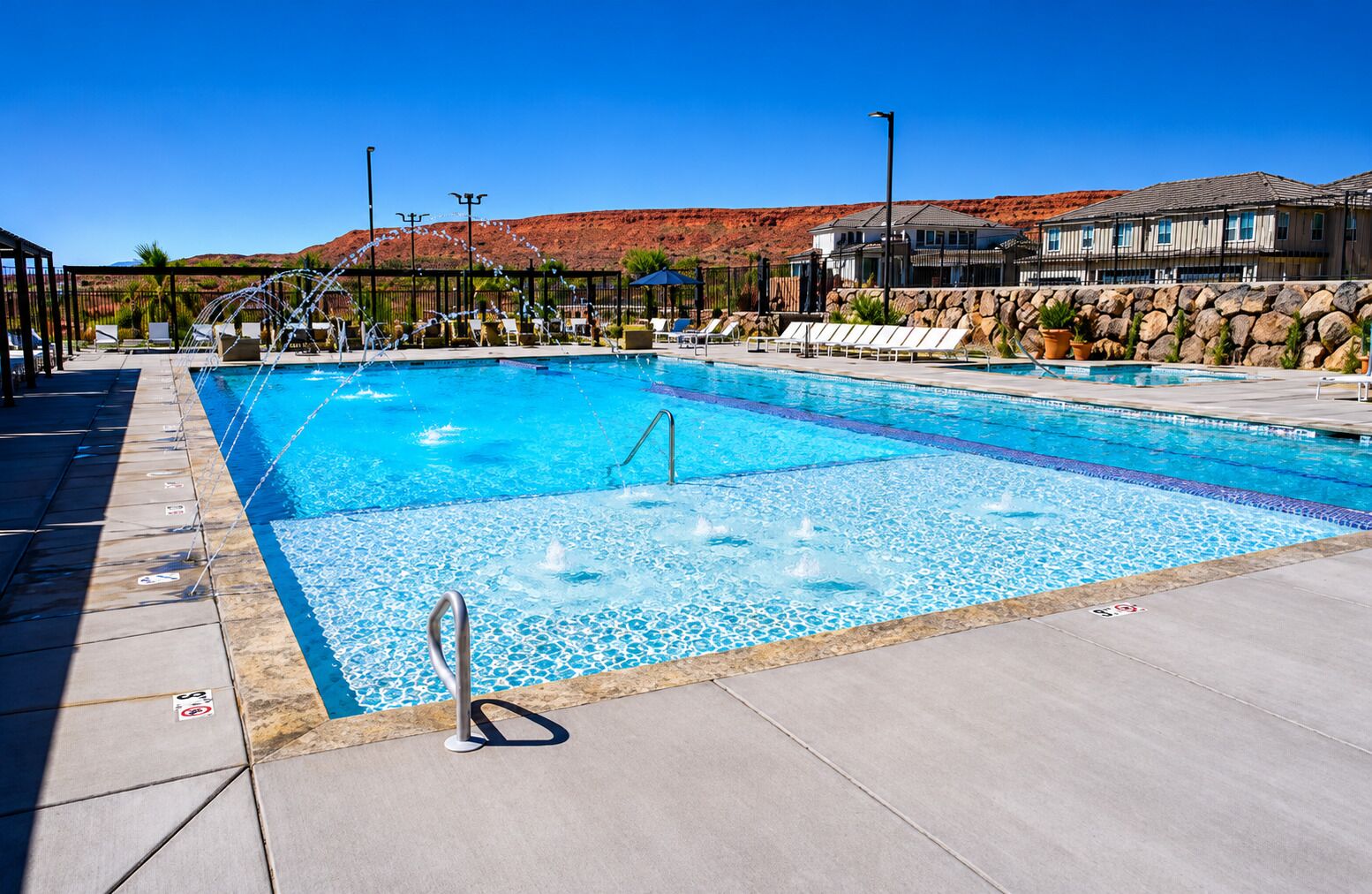 A swimming pool with a stone wall, lounge chairs, and a clear blue sky.