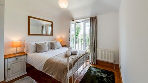A bedroom with a bed, bedside tables, a mirror, a radiator, and a window with curtains. - Cosy 3BR House with free parking (Oxford)