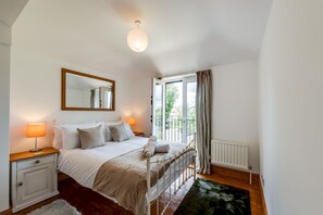 Ein Schlafzimmer mit einem Bett, Nachttischen, einem Spiegel, einem Heizkörper und einem Fenster mit Vorhängen.