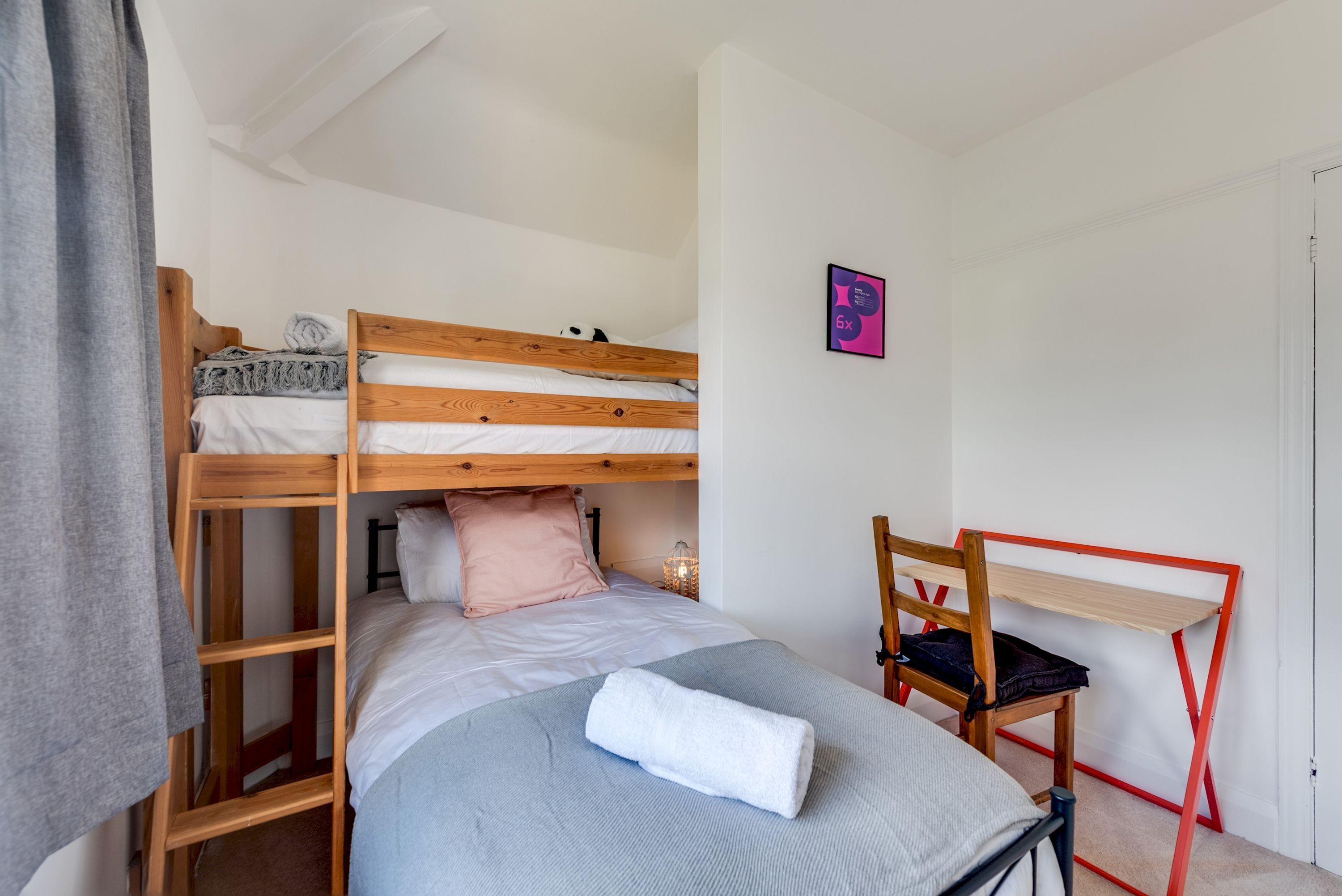 Un lit superposé avec une échelle, un bureau avec une chaise et une petite table de chevet avec une lampe.