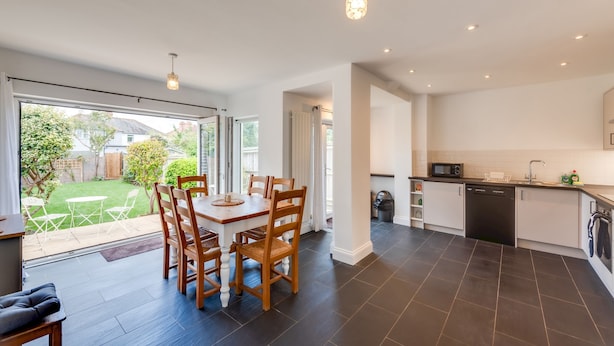 A modern kitchen with dark tiled flooring, a dining area with wooden chairs and a table, and a view of a garden through large sliding doors. - Cosy 3BR House with free parking (Oxford)