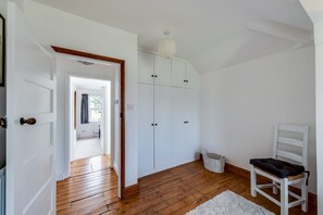 Ein Zimmer mit Holzboden, weißen Wänden, einer weißen Tür, einem weißen Stuhl und einem weißen Kleiderschrank mit einer Pendelleuchte.