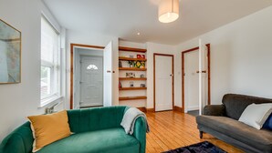 A living room with a green sofa, a grey sofa, wooden shelves with books, and a black rug. - Cosy 3BR House with free parking (Oxford)