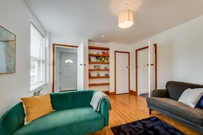 Ein Wohnzimmer mit einem grünen Sofa, einem grauen Sofa, Holzregalen mit Büchern und einem schwarzen Teppich.