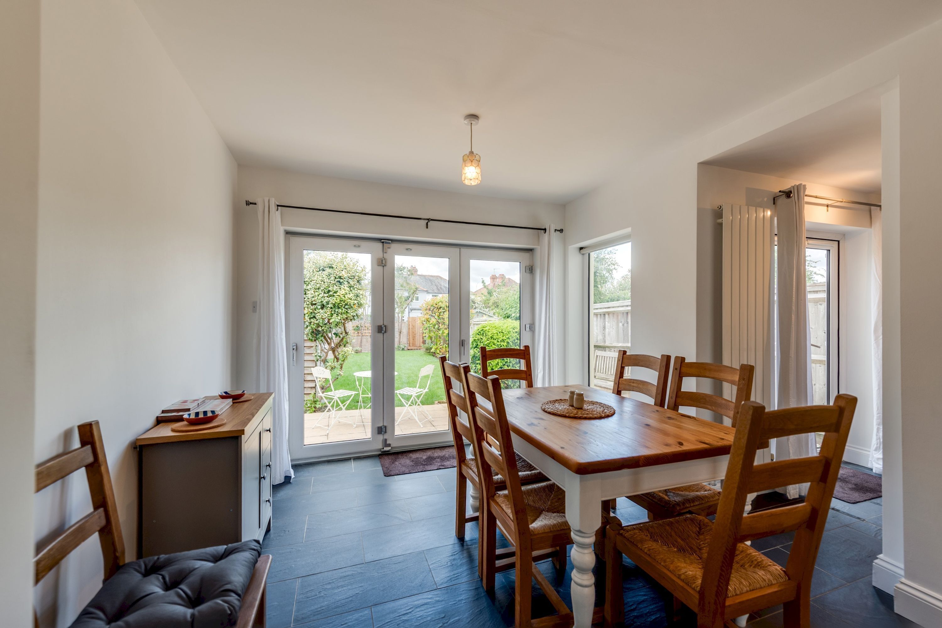 A dining area with a wooden table and chairs, a bench, and a view through glass doors to a garden.