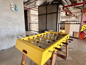 Ein Kicker in einem Raum mit Betonboden, Metallträgern und einem großen Fenster.