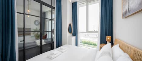 A hotel room with a large bed, a view through a sliding door, a bedside table with a lamp, and a wall clock.
