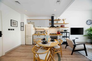 Een moderne keuken met een eethoek, houten stoelen, een flatscreen televisie en een klok aan de muur.