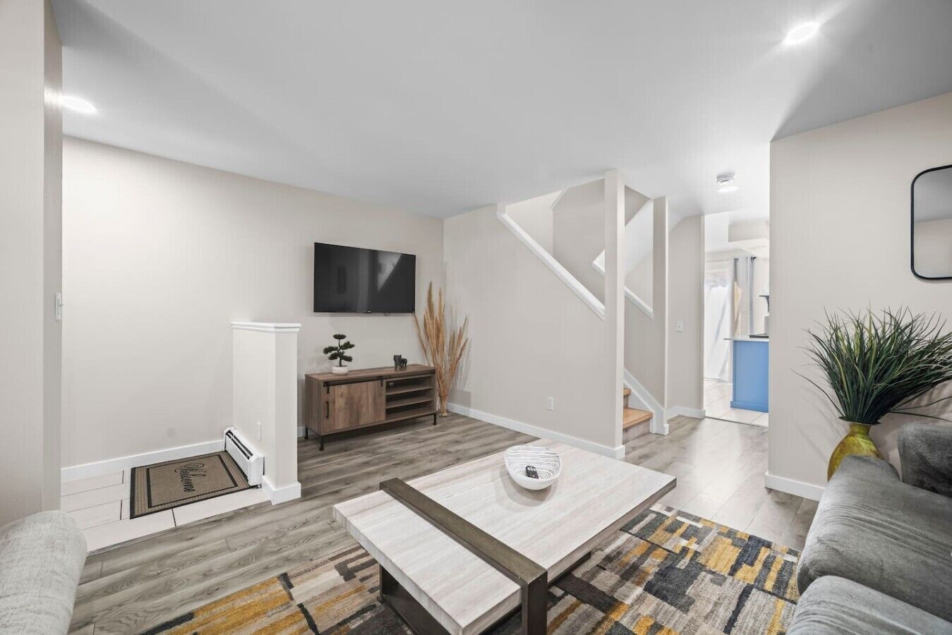 A modern living room with a sofa, coffee table, TV, and a staircase leading to another level.