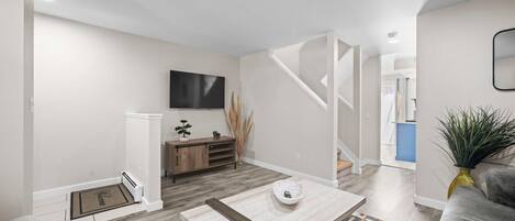 A modern living room with a sofa, coffee table, TV, and a staircase leading to another level.