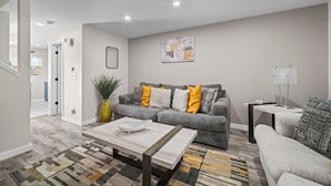 Ein Wohnzimmer mit grauem Sofa, einem Couchtisch, einem gemusterten Teppich und einer Pflanze.