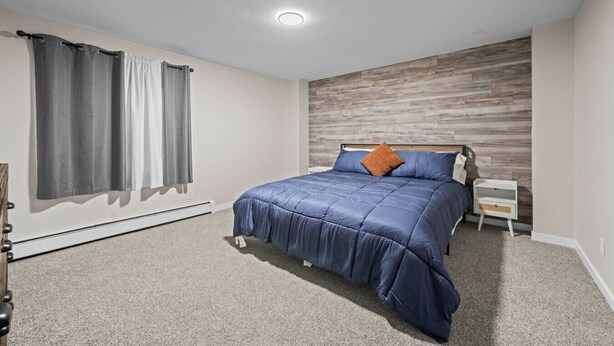 Ein Schlafzimmer mit Bett, Nachttisch, einer Wand mit Holzvertäfelung und einem Fenster mit Vorhängen.