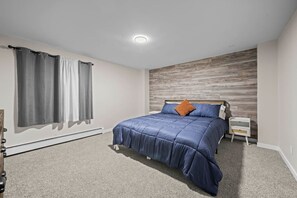 Een slaapkamer met een bed, een nachtkastje, een houten accentmuur en een raam met gordijnen.